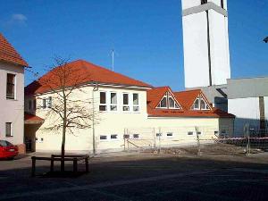 Bild: hintere Teilansicht des Gerätehauses vom Schulhof (im Hintergrund: die kath. Pfarrkirche Wiesbach)