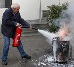 Bild: Die Handhabung eines 12-kg-Feuerlöschers (Bruttogewicht ca. 20 kg) ist nicht sehr einfach (Foto KI-generiert),.....